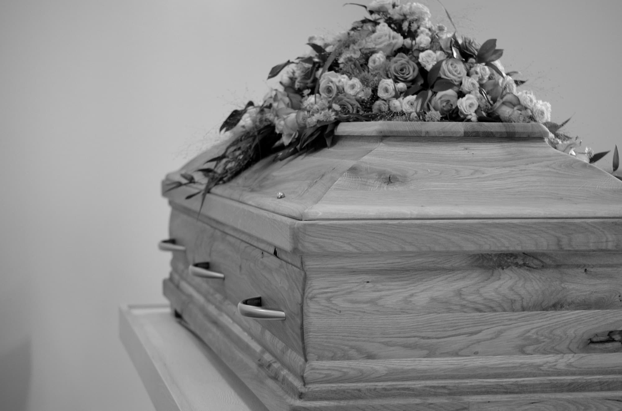 Un ataúd con un arreglo floral, fotografiado en blanco y negro